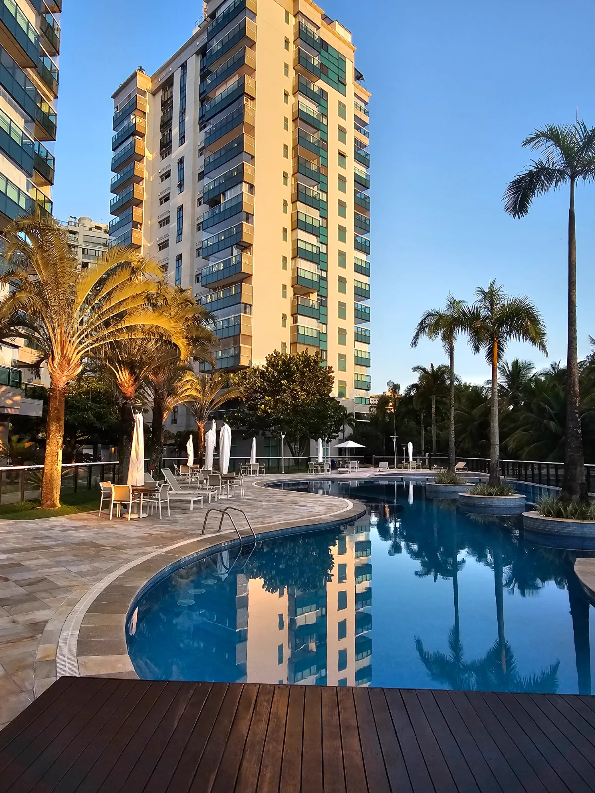 Piscina do condomínio ao entardecer com fachada do prédio